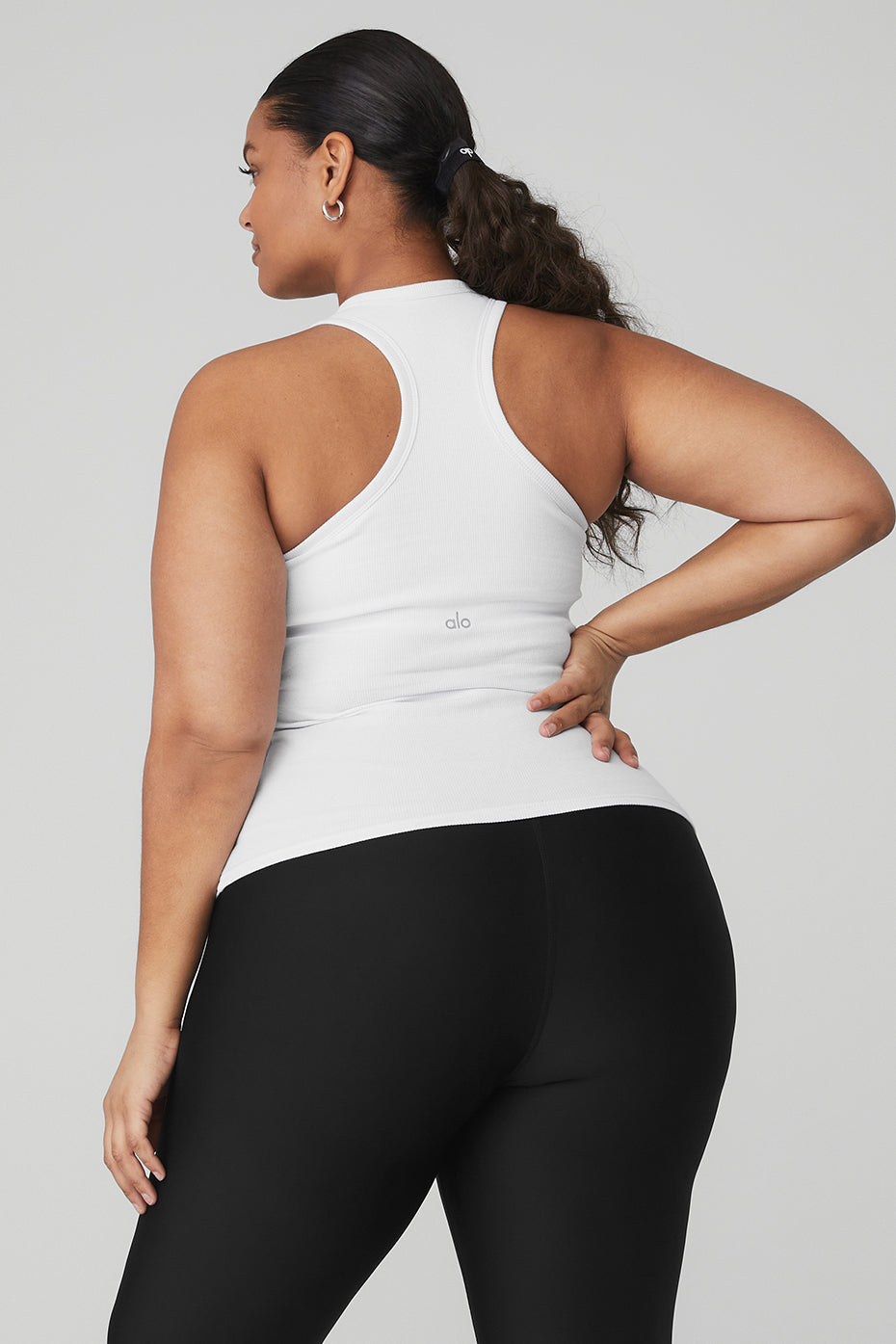 Back view of a woman wearing a white Ribbed Aspire Full Length Tank with a racerback and black leggings.