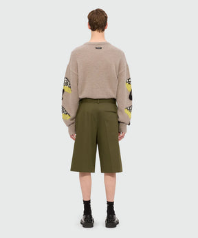 Back view of male model wearing olive green cotton drill Bermuda shorts with pleats and MSGM logo, paired with a beige sweater.