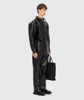 Male model wearing black long-sleeved shirt with structured faux leather pocket and matching pants, holding a tote bag.