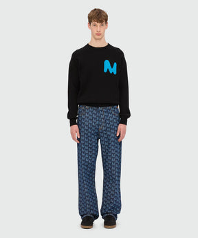 Model wearing blue laser-cut denim trousers with TheMwave motif and black sweatshirt featuring M logo.