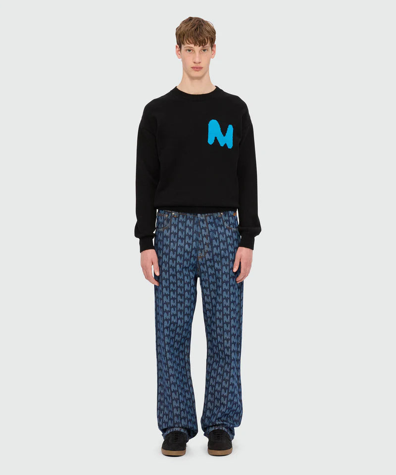 Model wearing blue laser-cut denim trousers with TheMwave motif and black sweatshirt featuring M logo.