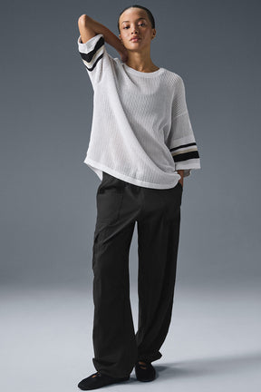 Model wearing an open knit playoff jersey with wide exaggerated arms in a boxy fit, paired with loose black pants.