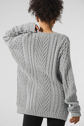 Back view of a gray cable knit crew neck sweater showcasing chunky knit detailing and a relaxed silhouette.