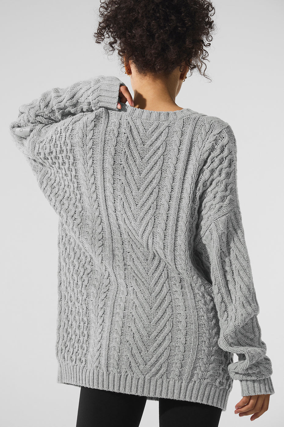 Back view of a gray cable knit crew neck sweater showcasing chunky knit detailing and a relaxed silhouette.