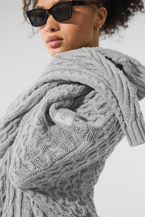 Gray cable knit crew neck sweater worn casually with sunglasses, showcasing chunky knit detailing and relaxed silhouette.