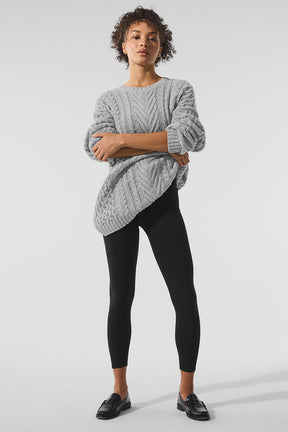 Woman wearing a gray cable knit crew neck sweater paired with black leggings for a chic casual look.
