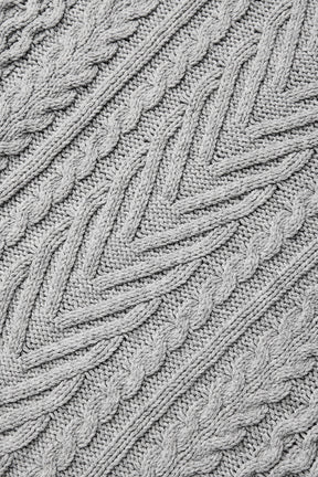 Close-up of a cable knit texture in a light gray color, showcasing chunky patterns of a crew neck sweater design.