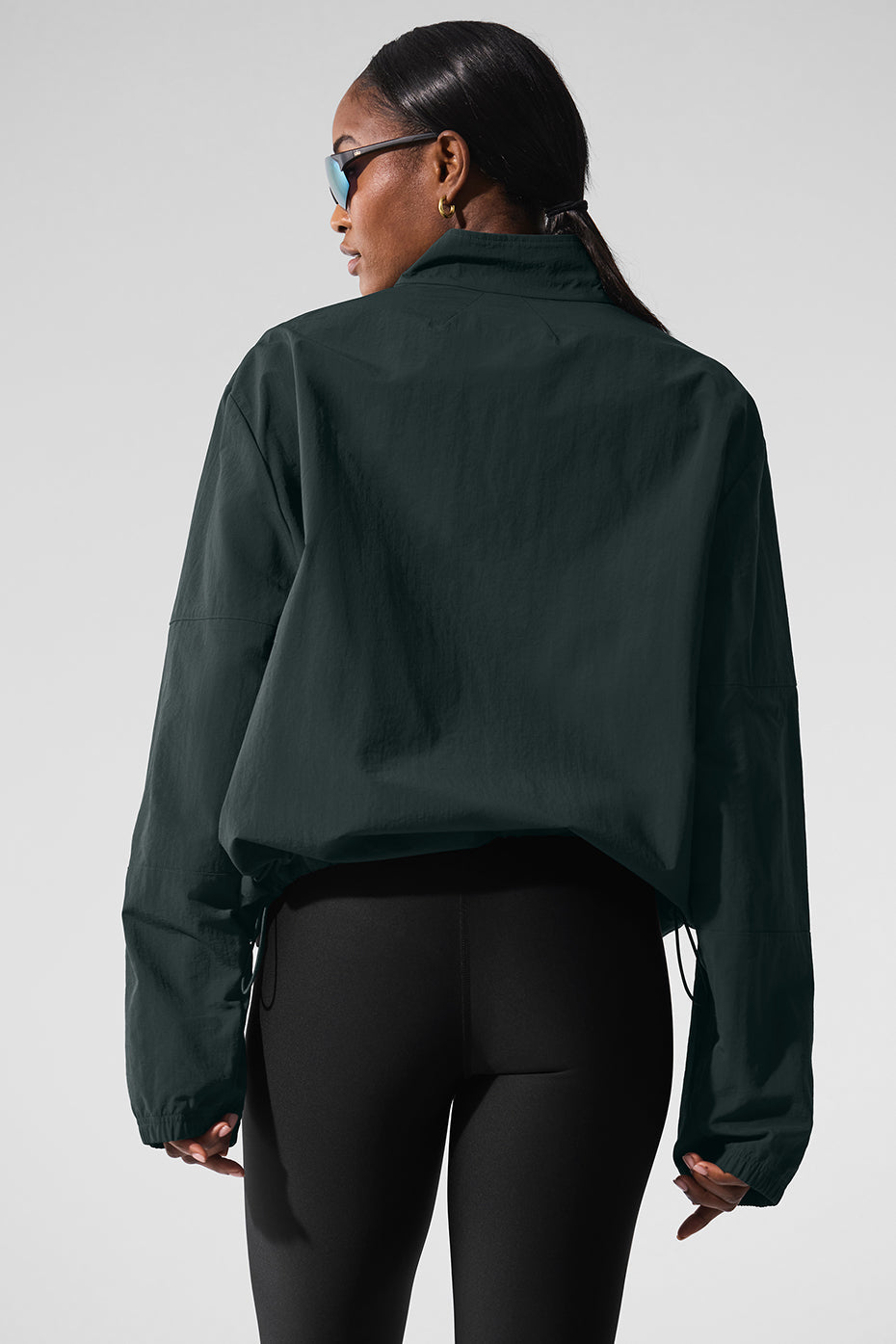 Back view of a woman wearing a light weight takeaway track pullover with quarter-zip neck and zippered pockets.