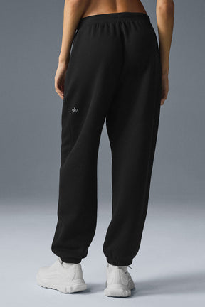 Back view of a person wearing black cozy sweatpants with zippered pockets and stretchy cuffs.