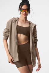 Model wearing Renown Full Zip Hoodie with sporty sunglasses over a brown crop top and shorts, showcasing casual athleisure style.