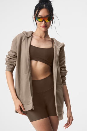 Model wearing Renown Full Zip Hoodie with sporty sunglasses over a brown crop top and shorts, showcasing casual athleisure style.