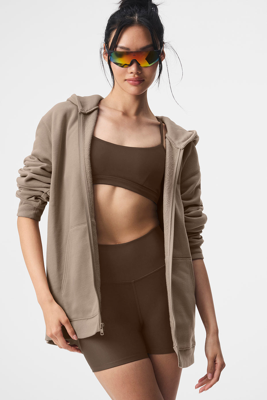 Model wearing Renown Full Zip Hoodie with sporty sunglasses over a brown crop top and shorts, showcasing casual athleisure style.