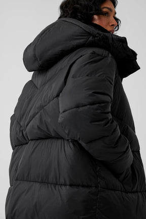 Model in oversized black puffer coat featuring a hood, showcasing winter outerwear style for chilly weather.