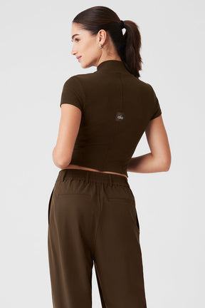 Back view of a woman wearing a Wellness Rib Mock Neck Polished Short Sleeve top with contour seaming and stylish trousers.