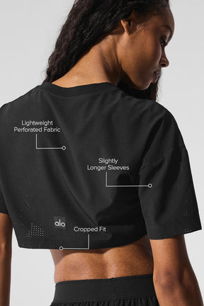 Back view of a model wearing the Mesh Cropped Mirage Tee showcasing lightweight perforated fabric and slightly longer sleeves.