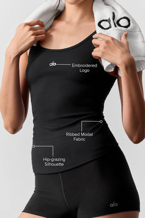 Model wearing a black ribbed modal tank top showcasing embroidered logo and hip-grazing silhouette.