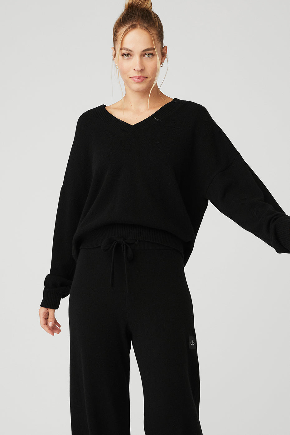 Model wearing a black Cashmere Jet Set V-Neck Pullover with dropped shoulders and ribbed cuffs, styled with matching pants.