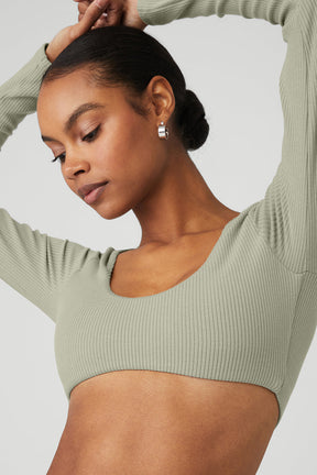 Model wearing a ribbed defined long sleeve bra in soft green, featuring a scoop neck and cropped design.