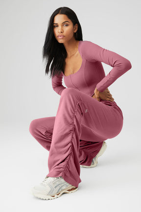 Model wearing ALO Softsculpt long sleeve crop top with matching ruched pants in pink, showcasing street-style vibes.