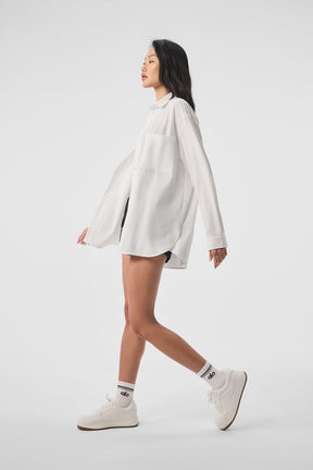 Model wearing Dreamscape Button Down Long Sleeve in white, showcasing its oversized fit and front pockets.