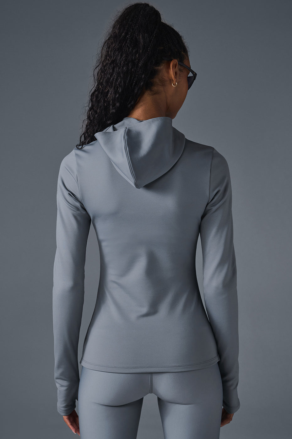 Back view of a woman wearing a gray Airlift Winter Warm Hooded Runner, showcasing its sleek design and built-in hood.