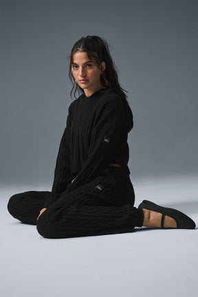 Model wearing a black cable knit Winter Bliss Hoodie with matching pants, showcasing cozy winter fashion.