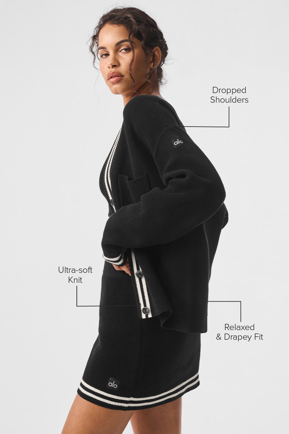 Model showcasing a Tennis Club sweater knit cardigan with dropped shoulders and relaxed fit in black with striped trim.