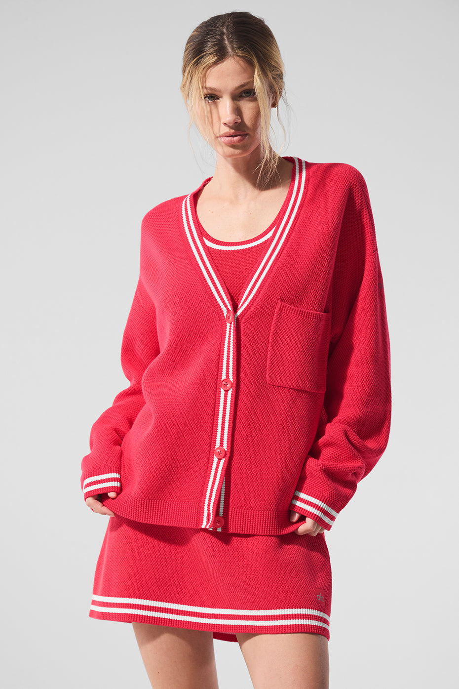 Model wearing a red Tennis Club sweater knit cardigan with striped trim and a matching skirt, showcasing a stylish look.