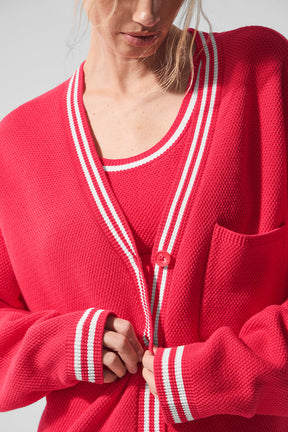 Woman wearing a pink Tennis Club sweater knit cardigan with striped trim and buttons, showcasing a stylish casual look.