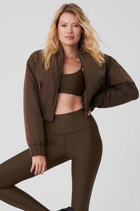 Model wearing a cropped break line bomber jacket made from memory woven fabric in brown, paired with matching activewear.