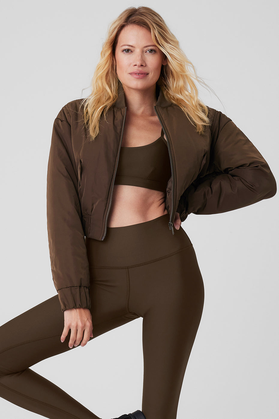 Model wearing a cropped break line bomber jacket made from memory woven fabric in brown, paired with matching activewear.