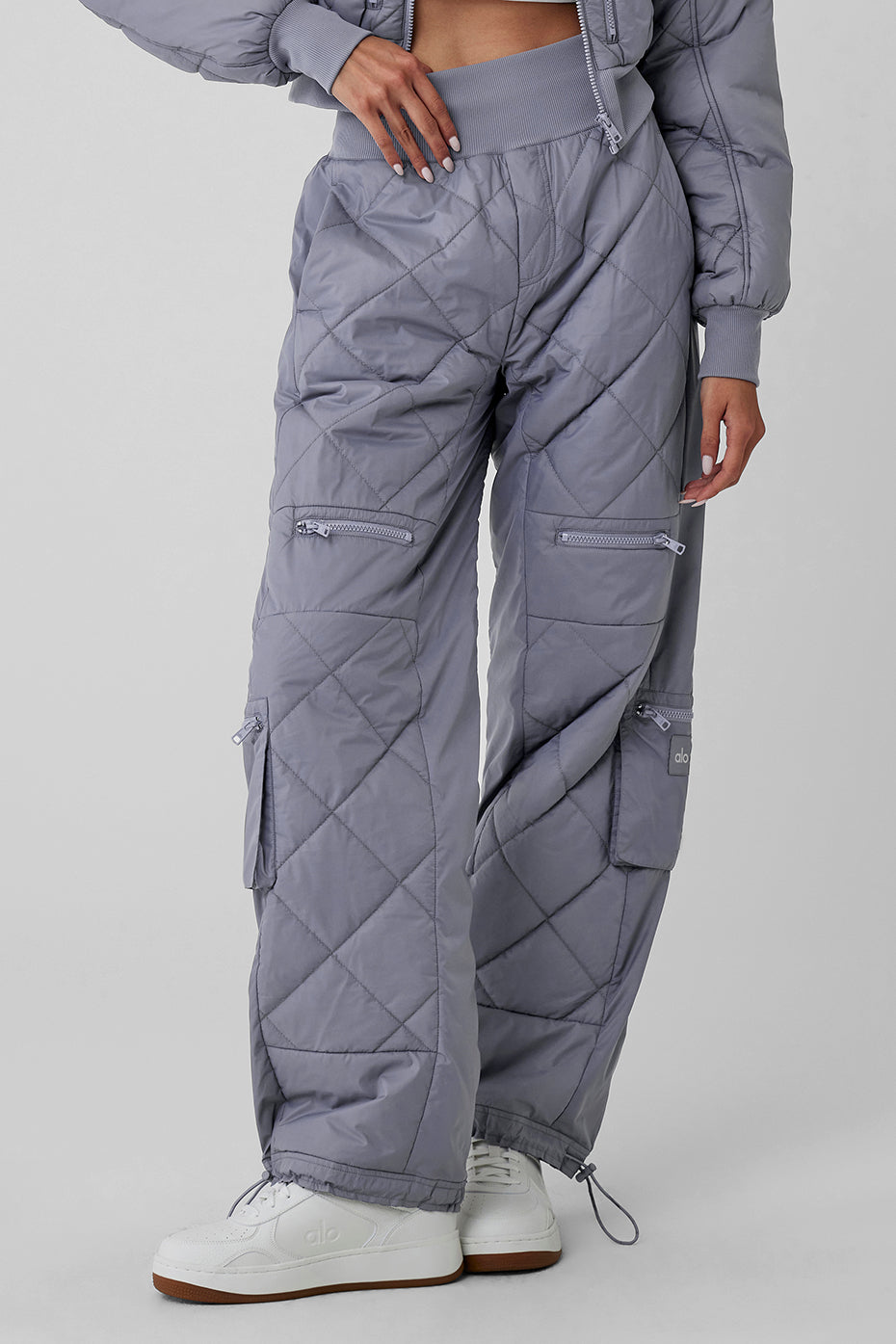 High-waist puffer pants in quilted grey with ribbed waistband and multiple zippered pockets for a trendy snowy look.