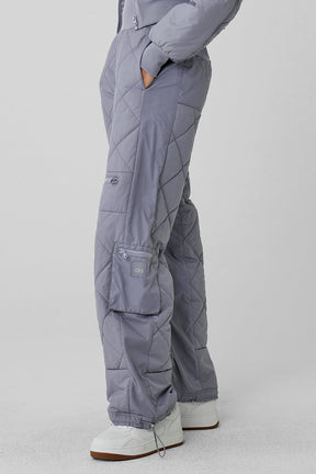 High-waist Snowrider puffer pant in gray, featuring quilted finish, wide ribbed waistband, and multiple zippered pockets.