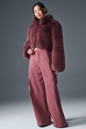 Opulent faux fur cropped jacket in a rich burgundy color, styled with wide-leg pants, exuding elegance and chic fashion.