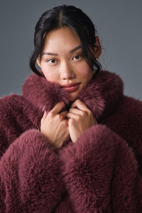 Model wearing an opulent faux fur cropped jacket with a stand collar in rich burgundy, showcasing its chic, fluffy texture.