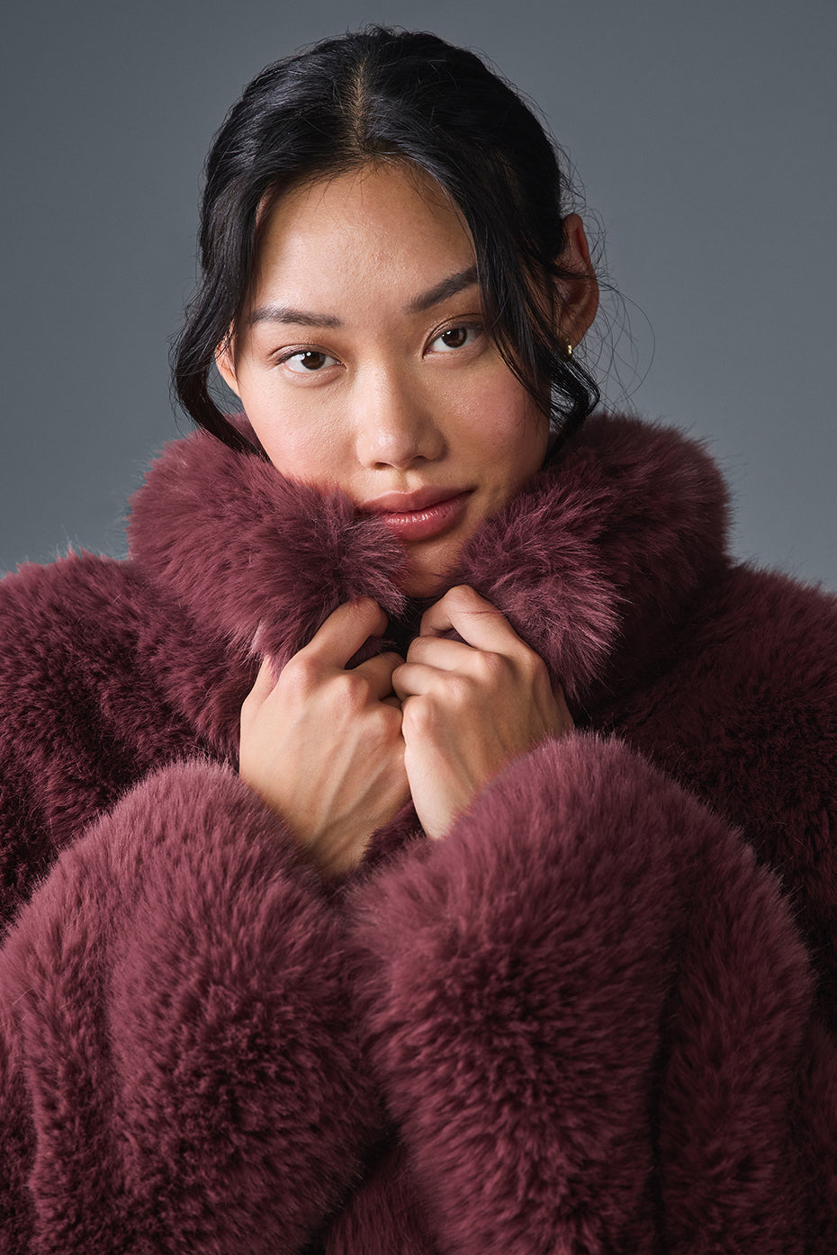 Model wearing an opulent faux fur cropped jacket with a stand collar in rich burgundy, showcasing its chic, fluffy texture.