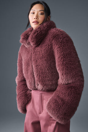 Opulent faux fur cropped jacket with a stand collar in soft pink on a model styled with elegant pants.