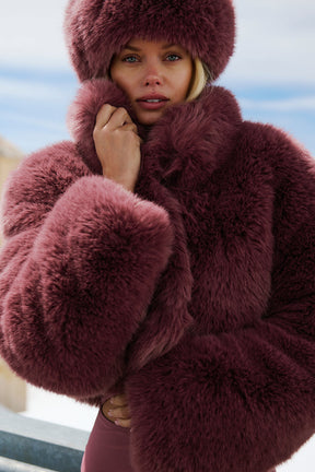 Opulent faux fur cropped jacket in burgundy worn stylishly, featuring a boxy shape and stand collar, perfect for chic looks.