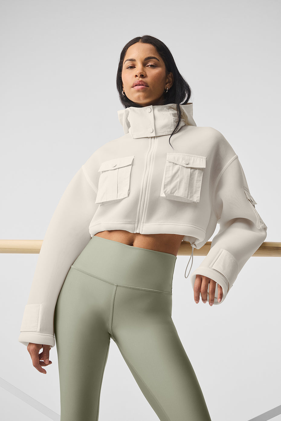 Cropped Engage Cargo Parka in white with cargo snap pockets, hood, and boxy silhouette, styled with form-fitting leggings.