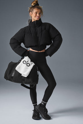 Model wearing Main Act Corset Puffer jacket with cropped silhouette and black leggings, holding a gym bag.