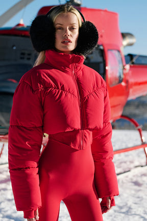 Model wearing a red Main Act Corset Puffer jacket in snowy landscape, showcasing its cropped silhouette and warm design.