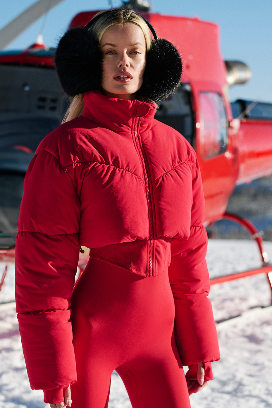 Model wearing a red Main Act Corset Puffer jacket in snowy landscape, showcasing its cropped silhouette and warm design.