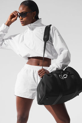Model wearing a white cropped pullover and Alumni Shorts, carrying a black duffel bag for sports and outdoor activities.