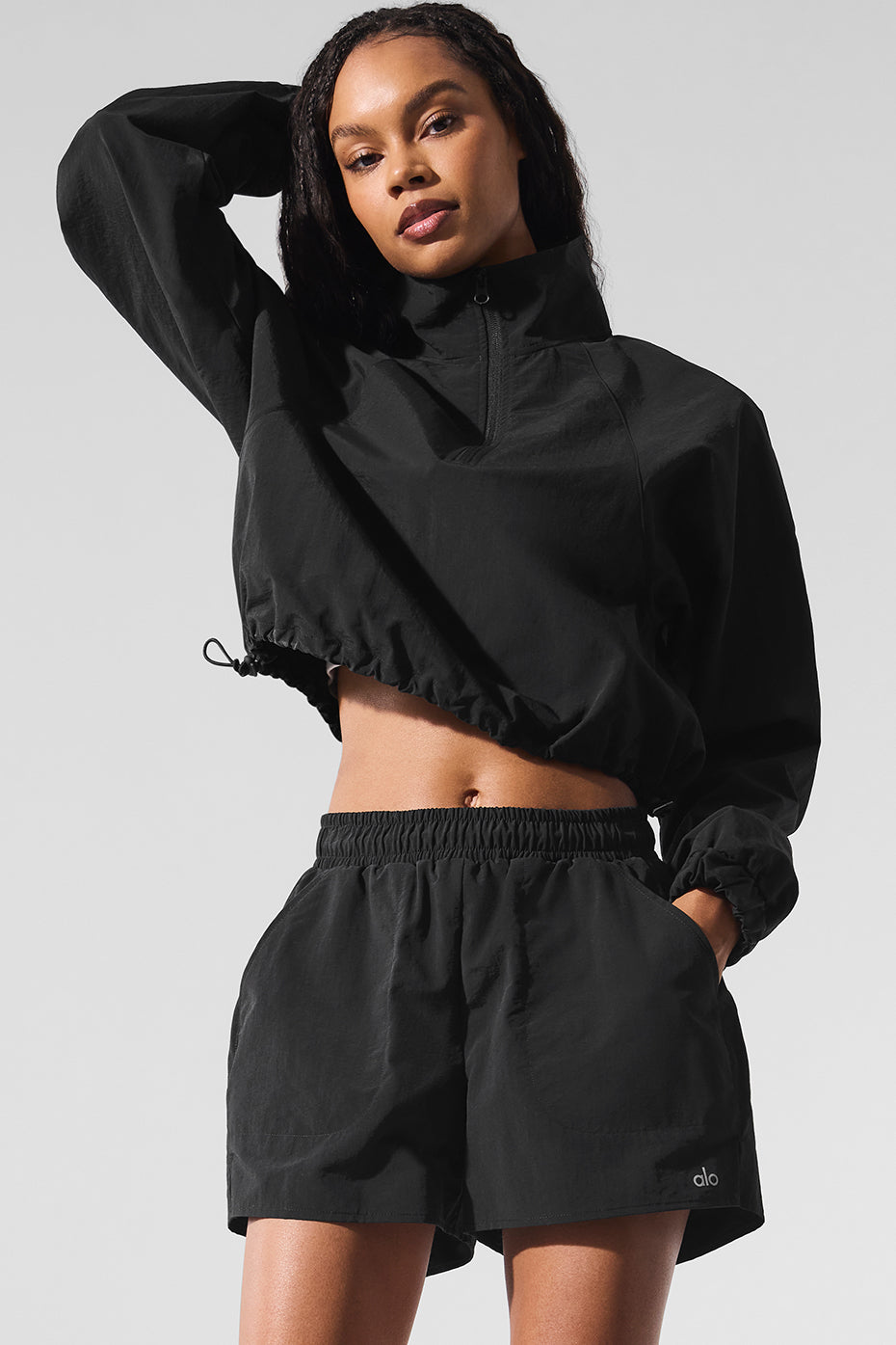 Woman wearing black cropped pullover and Alumni Short, showcasing high-waist design and lightweight fabric for active lifestyles.