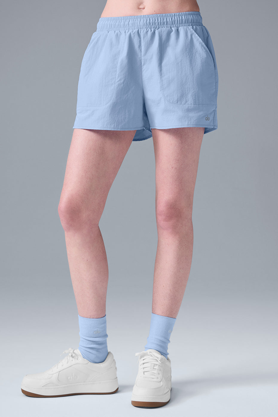 High-waist lightweight Alumni Short in light blue, designed for comfort with pockets for essentials and paired with sporty shoes.