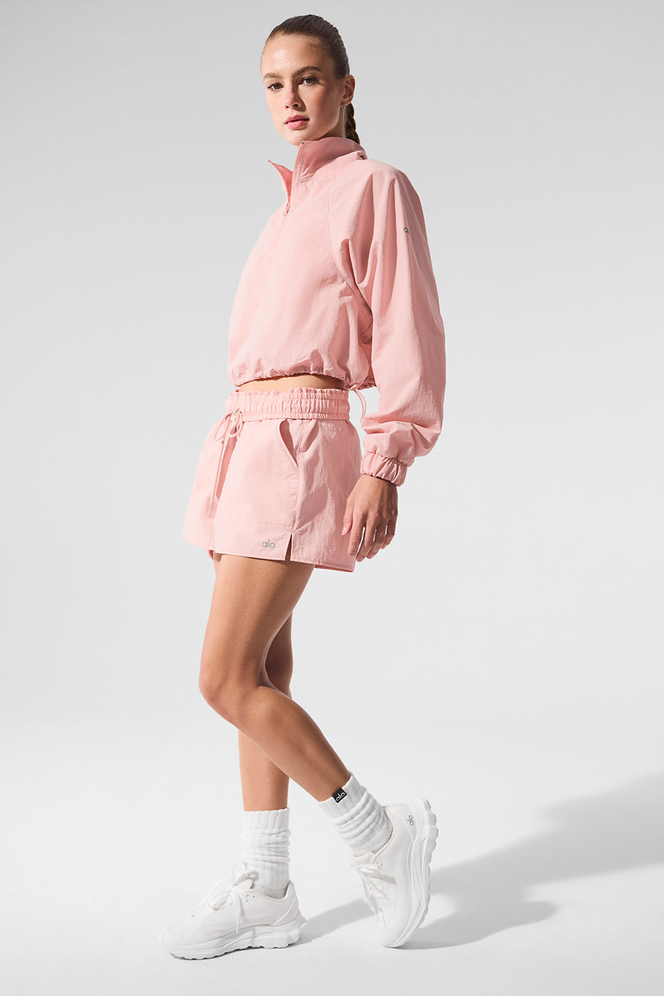Alumni Short in pink, high-waist design with internal drawcord, paired with matching cropped pullover and white sneakers.