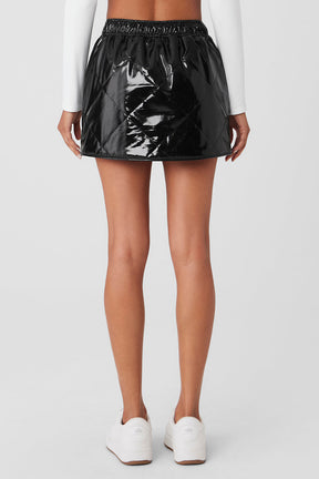 Back view of a model wearing the Snomoto Puffer Mini Skirt in high-shine black with a quilted finish.