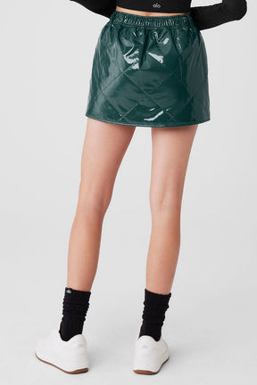 Model wearing a high-shine green quilted puffer mini skirt with high-rise waistband and mid-thigh length.