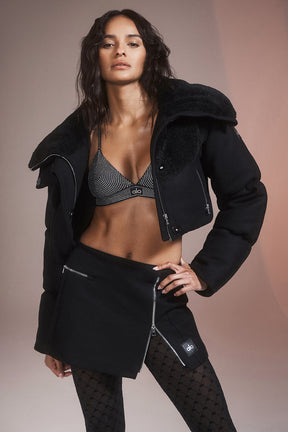 Model wearing a black cropped jacket with a shearling collar and a mini skirt, showcasing a chic winter look.