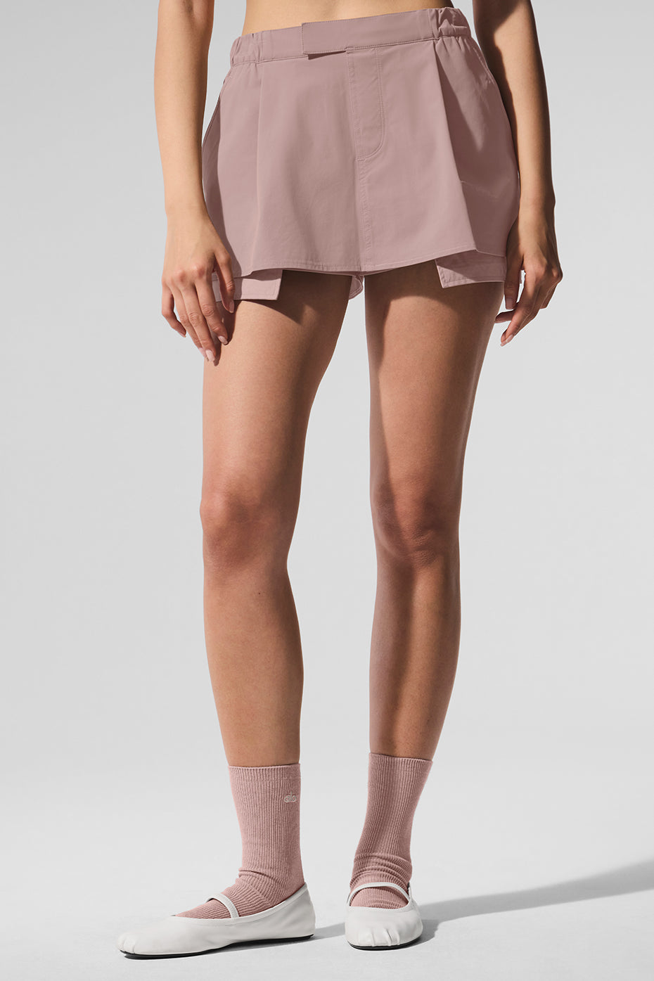 Model showcasing the Flip It Mini Skort featuring a low-waisted design and an elastic waistband in a soft pink color.